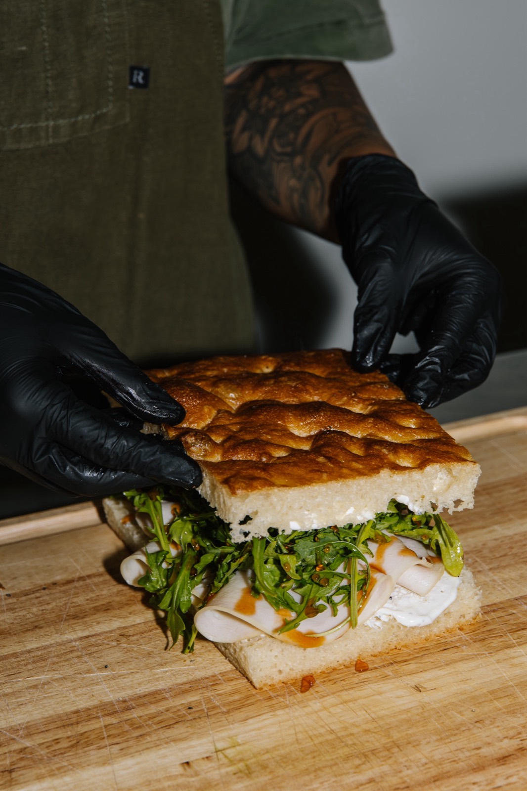 Hands placing focaccia on a fresh Hall Pass sandwich